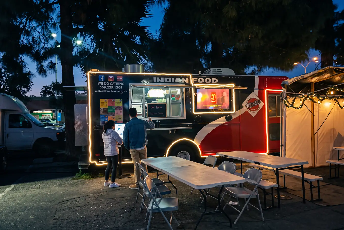 The Mumbai Express food truck lit up at dusk on El Camino Real, tables set out in front
